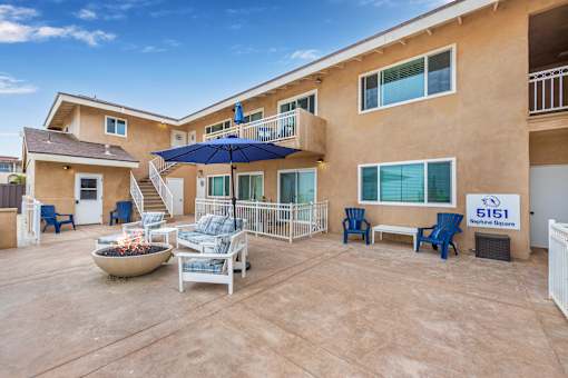 A patio at Neptune with a fire pit and chairs is surrounded by apartment buildings.
