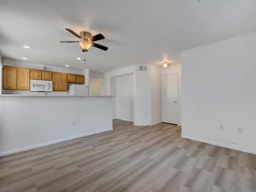 a living room with a ceiling fan and a kitchen in the background