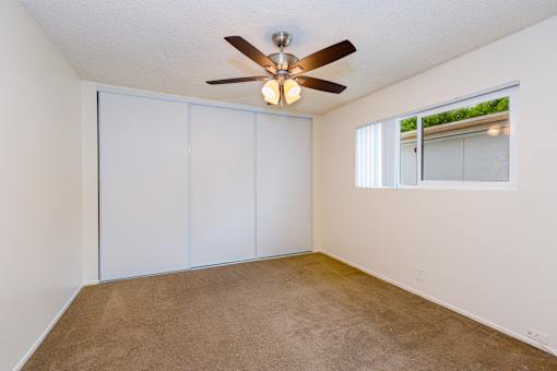 A bedroom with a ceiling fan and sliding closet doors.