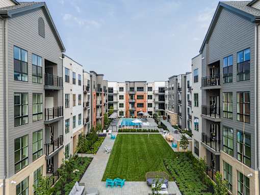 A view of a courtyard with a lawn and seating area surrounded by apartment buildings.