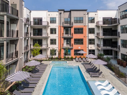 an outdoor pool with lounge chairs and umbrellas in front of an apartment building