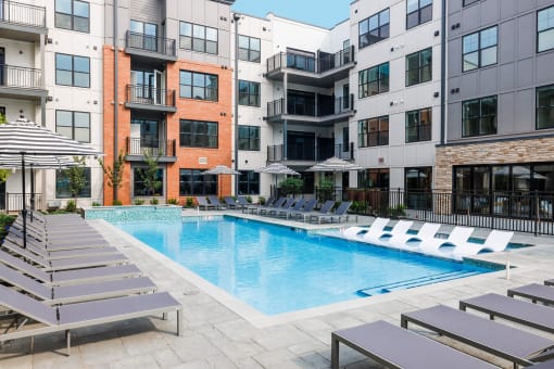a swimming pool with lounge chairs in front of an apartment building
