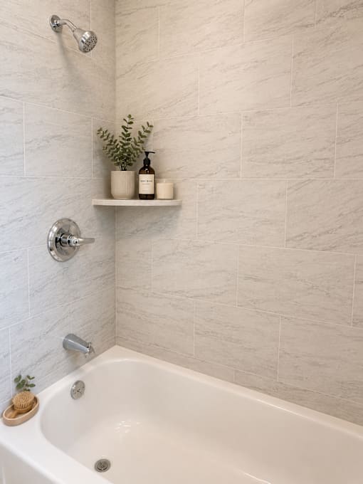 A white bathtub with a shower head and a shelf above it.