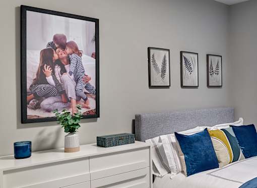 A bedroom with a large picture of a family on the wall above a bed with a grey headboard.