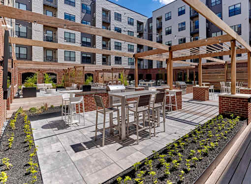 A patio with tables and chairs is surrounded by a brick wall and a wooden pergola.