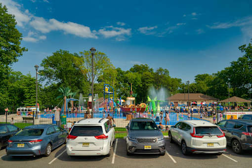 A parking lot with several cars and a playground in the background.