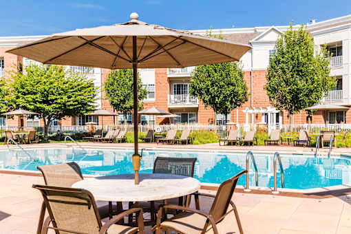 Poolside patio table with umbrella and lounge chairs at Highlands at Hilltop Apartments, Verona