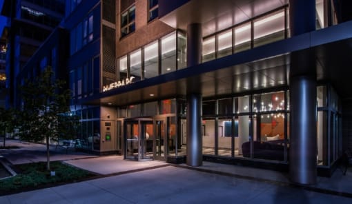 Building entrance with modern glass facade at night at RiverParc Apartments, New Jersey, 07086