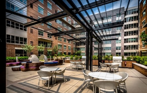 Covered outdoor patio with dining tables and planters at RiverParc Apartments, Weehawken, 07086