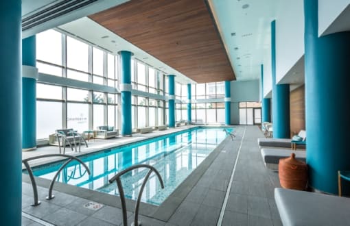 Indoor pool with lounge seating and large windows at RiverParc Apartments, Weehawken, NJ 07086