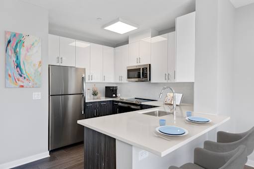 A modern kitchen with a refrigerator, microwave, and a counter with plates on it.