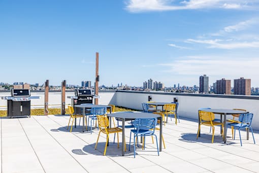 A rooftop patio with blue and yellow chairs and tables.