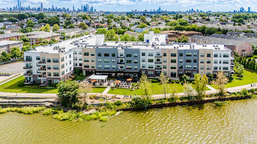Large apartment complex sits on the edge of a body of water with a city skyline in the background at The Waverton, Secaucus, NJ, 07094