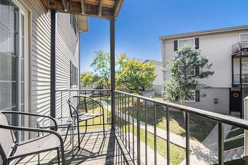 A balcony with a chair and a table overlooking a grassy area.