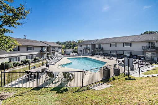 A swimming pool surrounded by a fence and chairs in a sunny day.