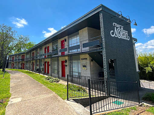 The Nolan Apartments building has a black fence and a green lawn in front.
