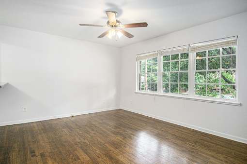 A room with a ceiling fan and a window with a view of trees.