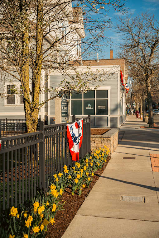 A building with a flag on a fence and yellow flowers in front.