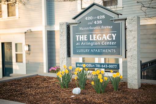 A sign for The Legacy at Arlington Center Luxury Apartments is displayed in front of a building.