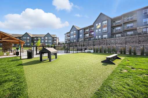 A grassy area in front of apartment buildings with a picnic table and a playground at The Garrison Luxury Apartment Homes, Fountain, CO 80817