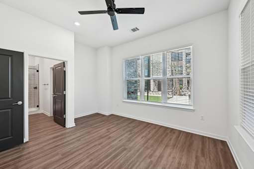 A room with a ceiling fan and a large window with blinds.