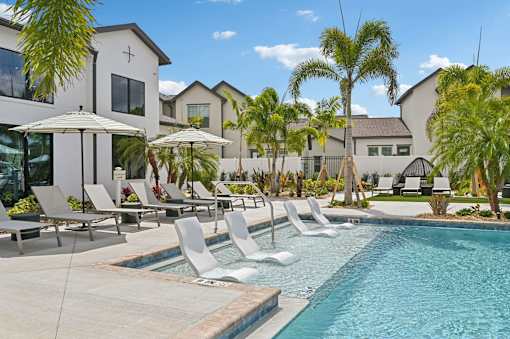 A pool with chairs and umbrellas in front of a building. at The Hadley - North Port, FL Apartments, North Port, Florida