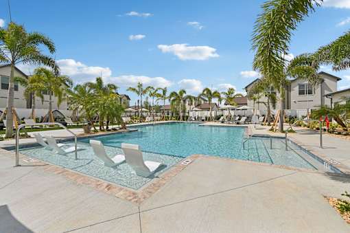 A swimming pool surrounded by palm trees and lounge chairs at The Hadley - North Port, FL Apartments, North Port