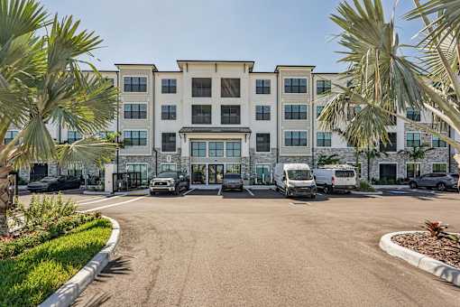 A parking lot in front of a multi-story building with palm trees at The Stadler Luxury Apartments, Florida