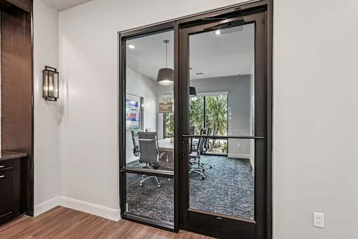 A glass door with a black frame leads to a room with a white wall and a brown cabinet at The Stadler Luxury Apartments, Florida