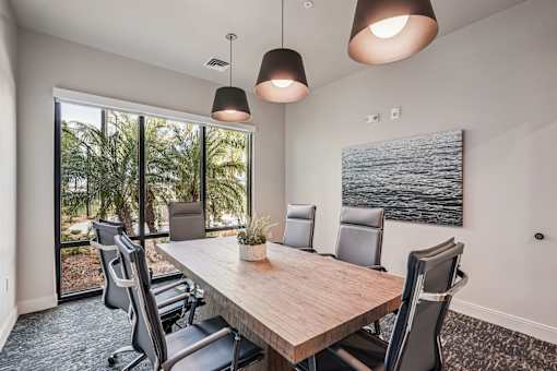 A conference room with a long table and chairs, a plant, and a painting on the wall at The Stadler Luxury Apartments, Bradenton, 34210