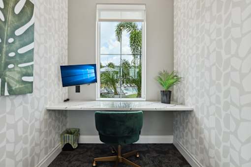 A white desk with a green chair and a blue monitor in front of a window.