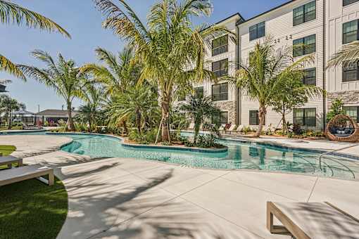 A pool surrounded by palm trees and a building in the background at The Stadler Luxury Apartments, Bradenton