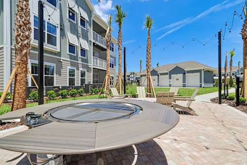 Outdoor fire pit with adirondack chairs and palm trees at Velara Luxury Apartments, Ponte Vedra Beach, FL