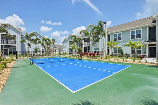 A tennis court is surrounded by apartment buildings.
