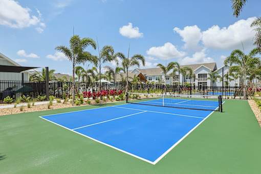 A blue tennis court surrounded by palm trees.