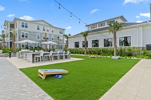 A patio area with a table and chairs is surrounded by a grassy area and a building in the background.