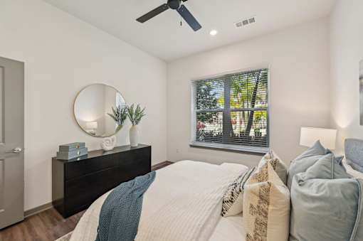 A bedroom with a large bed, a dresser, and a window with a view of trees.
