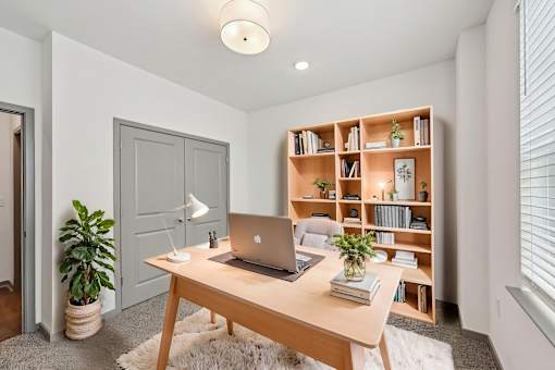 A room with a laptop on a desk and a bookshelf with various items. at The Sophia, Venice, FL