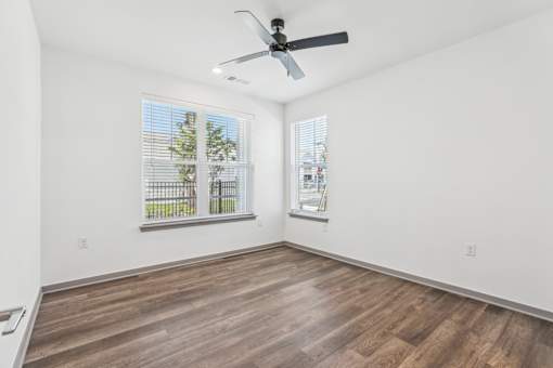 A room with a ceiling fan and two windows.