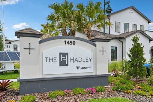 The Hadley sign is in front of a white building with a palm tree. at The Hadley - North Port, FL Apartments, North Port, FL