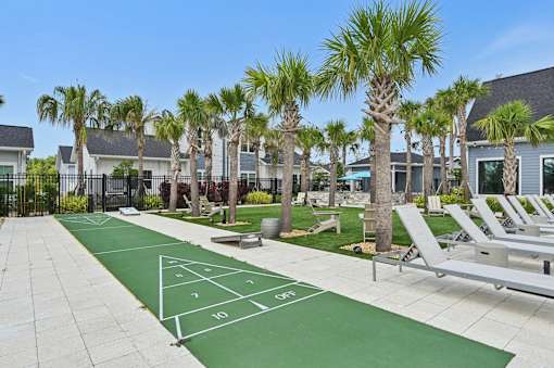 A tennis court is surrounded by palm trees and lounge chairs.