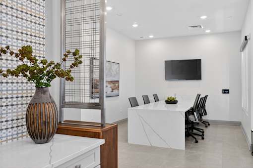 A conference room with a white table and chairs, a television on the wall, and a vase with green plants on the table.at Refinery at Pointe17 Apartments, Phoenix, AZ, 85085