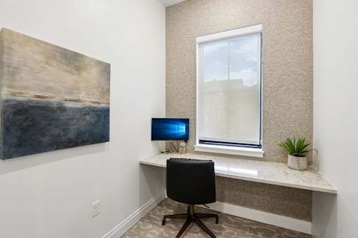 A room with a desk, chair, and a painting on the wall.
