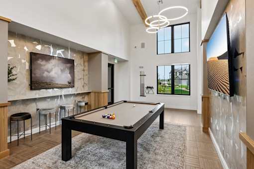 A pool table is in the middle of a room with a bar and a television.