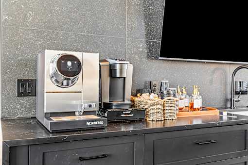 A Nespresso coffee machine sits on a countertop next to a basket of bread and some bottles.