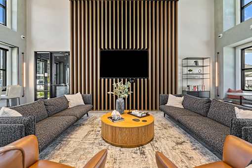 A modern living room with a large grey sofa, a wooden coffee table, and a TV mounted on the wall.