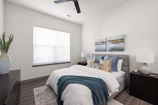 A bedroom with a bed, pillows, a ceiling fan, and two wall art pieces.
