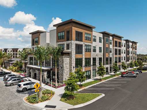 A row of modern apartment buildings with a parking lot in front.