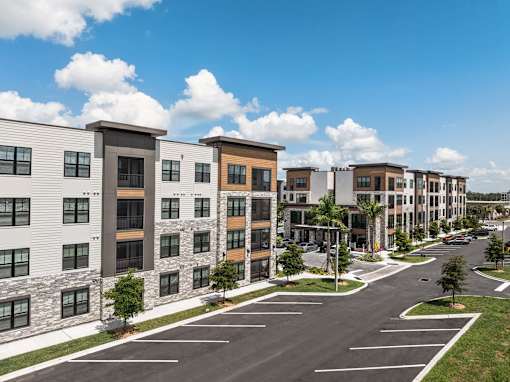 A row of modern apartment buildings with a parking lot in front.
