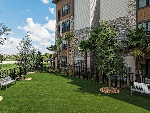 A large grassy area in front of a building with a bench and a tree.